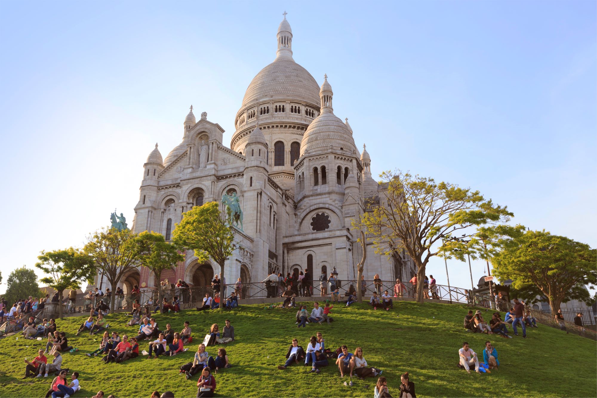 Photo de groupes de personnes assisent dans l'herbe devant la Basilique